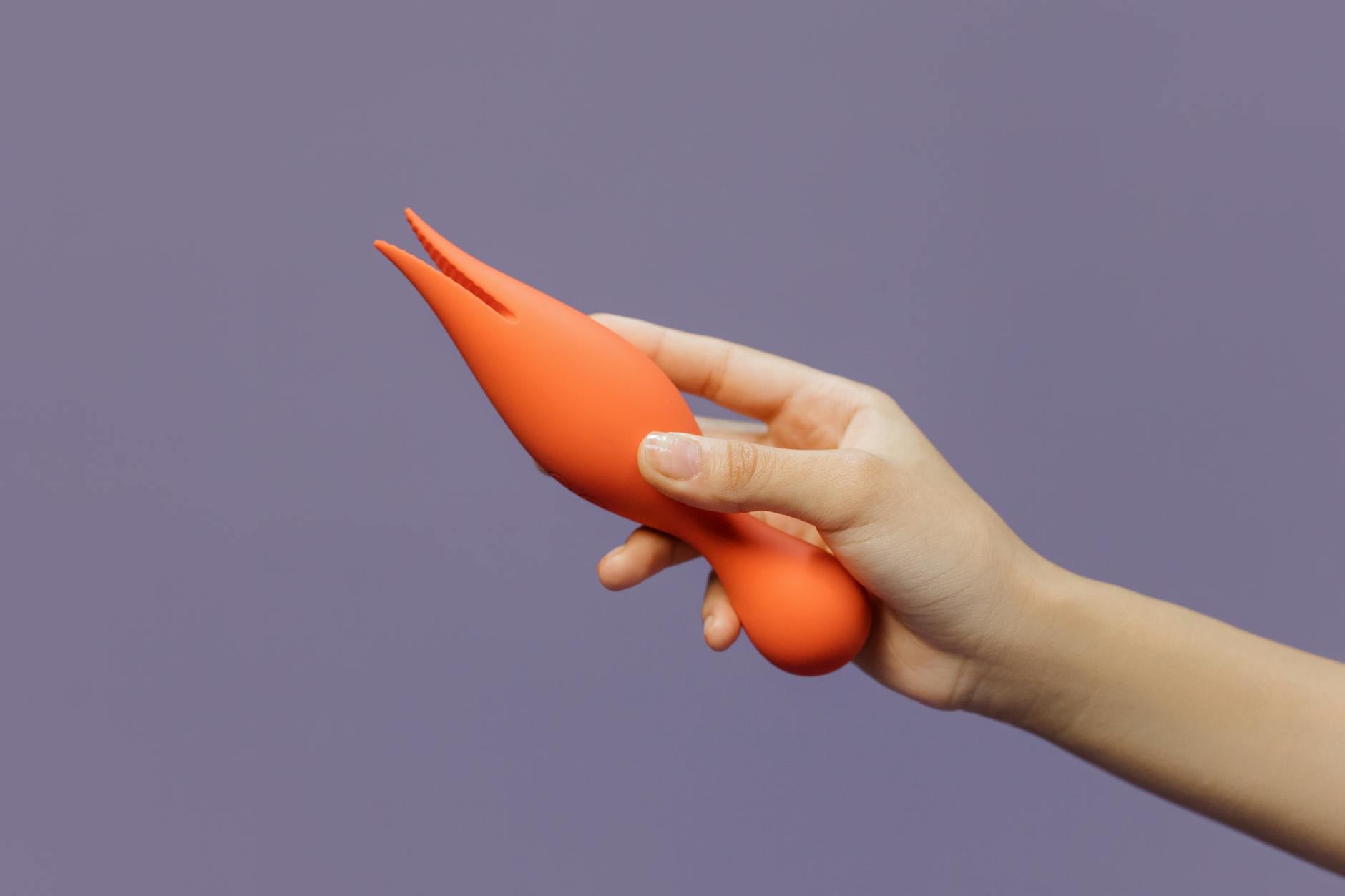 Close-up of a hand holding a vibrant lemon-colored vibrator against a minimalist purple backdrop