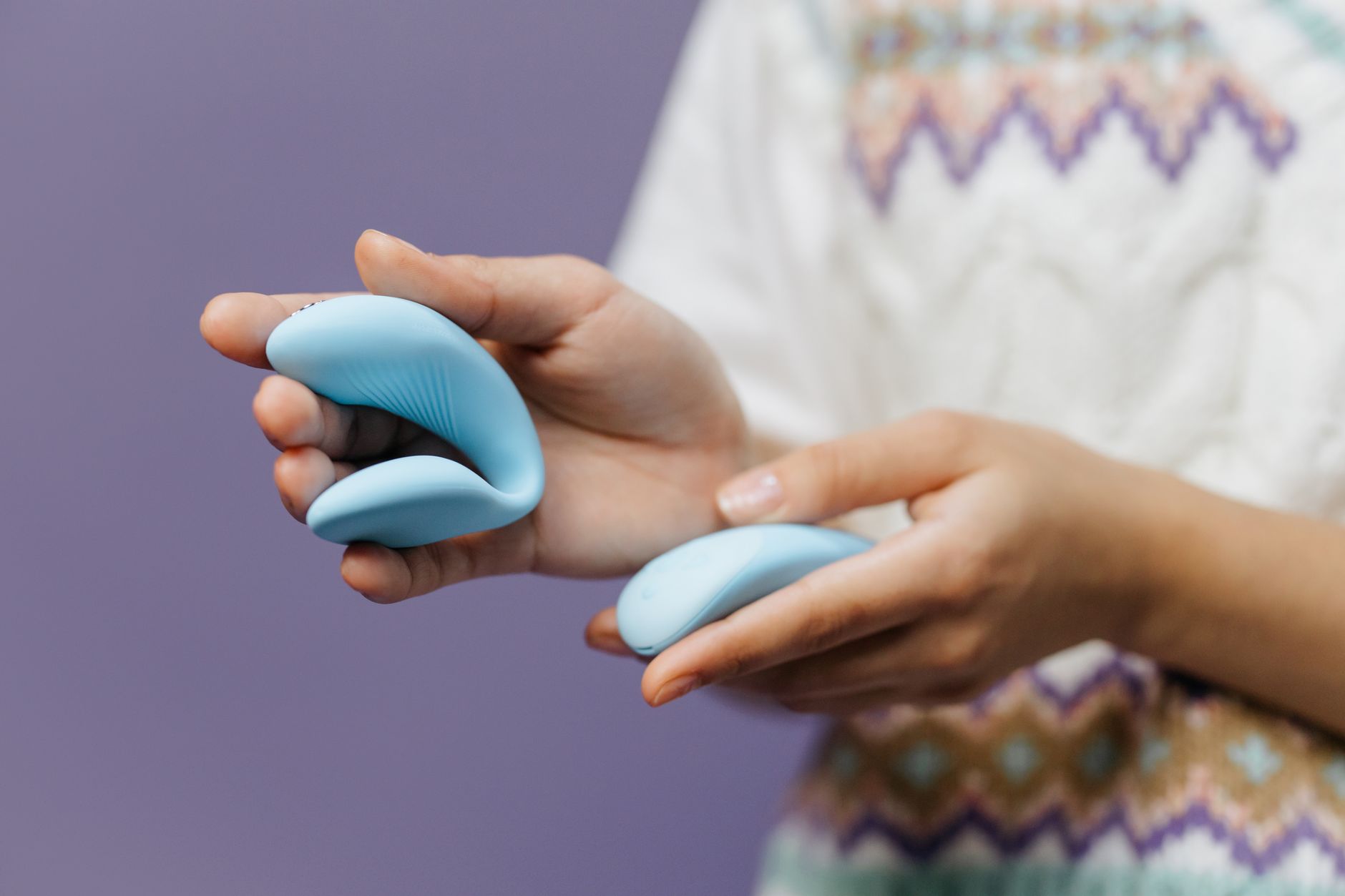 Close-up of hands holding a sleek lemon-colored vibrator against a purple background