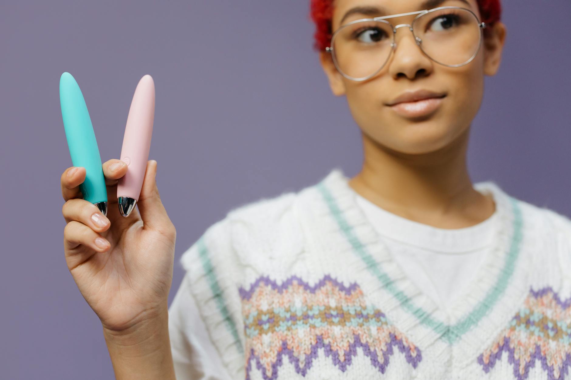 A woman holding colorful vibrators against a purple background, representing diverse pleasure options during recovery