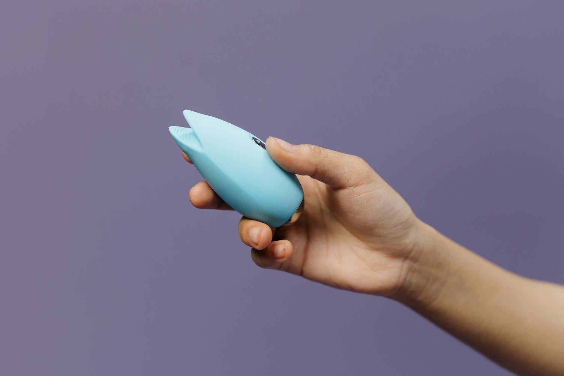 A blue silicone clitoral vibrator held in hand, representing solo pleasure and self-connection