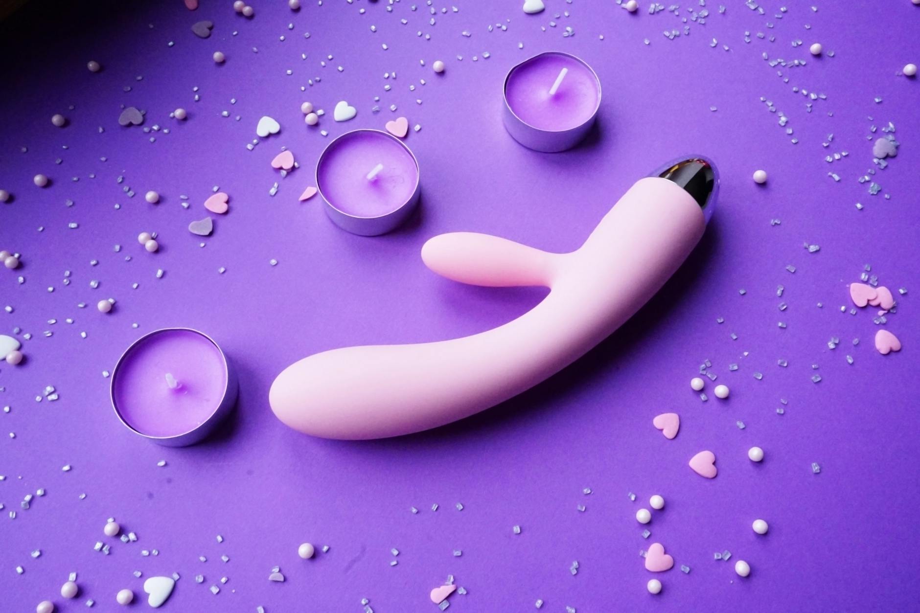 Pink vibrator on purple background with heart confetti and candles for intimate mood